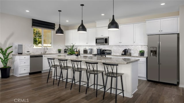 kitchen with a sink, white cabinetry, appliances with stainless steel finishes, a center island, and decorative light fixtures