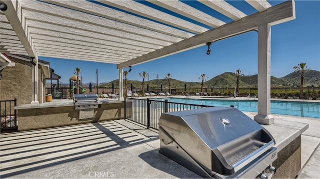 view of patio with a community pool, a mountain view, exterior kitchen, grilling area, and a pergola