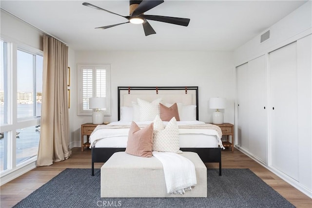 bedroom with baseboards, visible vents, wood finished floors, two closets, and ceiling fan