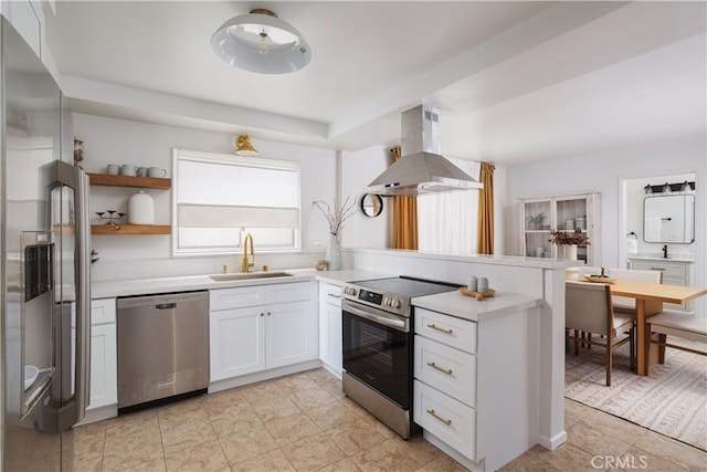 kitchen with island range hood, appliances with stainless steel finishes, light countertops, white cabinetry, and a sink