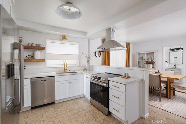 kitchen featuring a sink, island range hood, light countertops, a peninsula, and appliances with stainless steel finishes