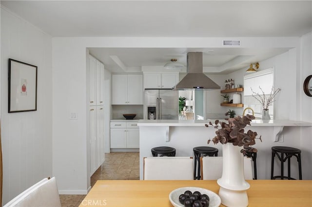 kitchen with island range hood, white cabinetry, a kitchen breakfast bar, light countertops, and stainless steel fridge with ice dispenser