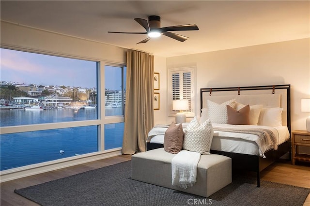 bedroom with a ceiling fan, wood finished floors, and a water view