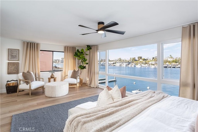 bedroom with access to outside, a water view, wood finished floors, and a ceiling fan