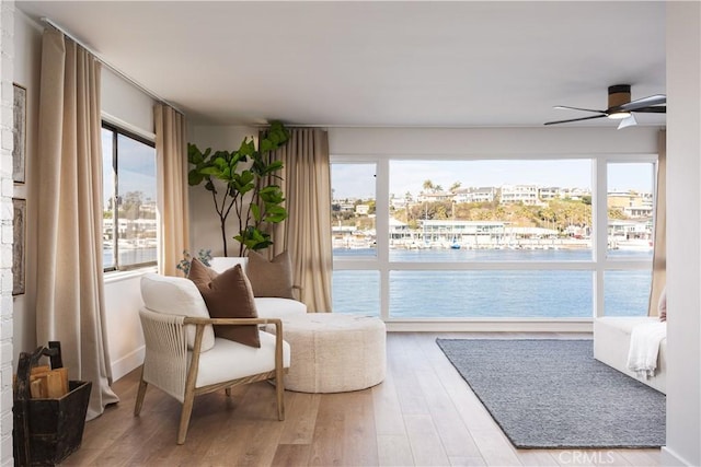 living area featuring ceiling fan, a water view, and wood finished floors