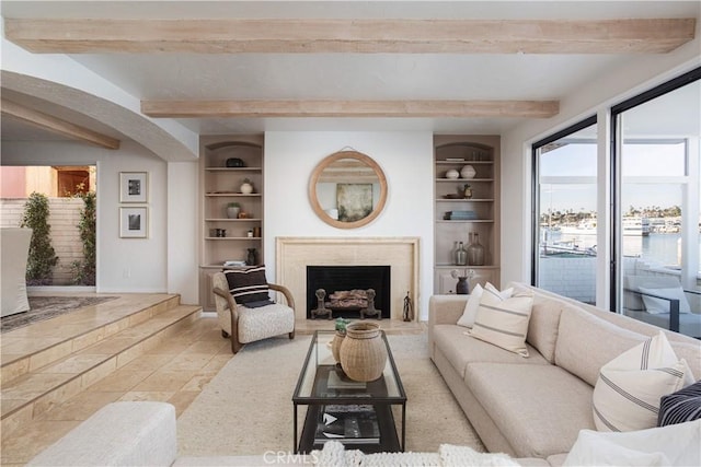 living area featuring a water view, built in shelves, a fireplace, and beam ceiling