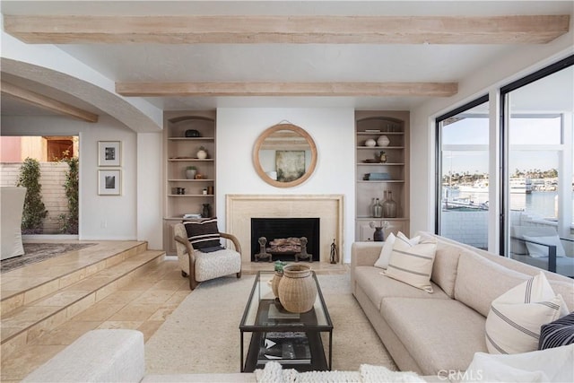 living area with built in shelves, arched walkways, beam ceiling, and a fireplace