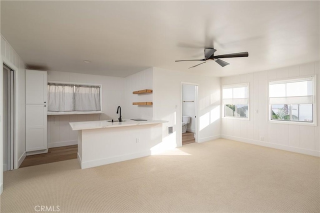 kitchen with light carpet, white cabinets, a peninsula, light countertops, and a sink