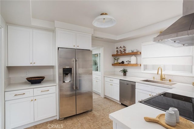 kitchen featuring wall chimney range hood, a sink, light countertops, white cabinets, and appliances with stainless steel finishes