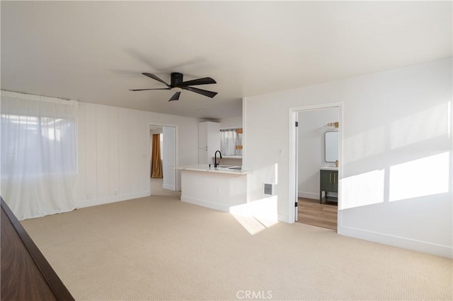 unfurnished living room with a sink, visible vents, baseboards, light colored carpet, and a ceiling fan
