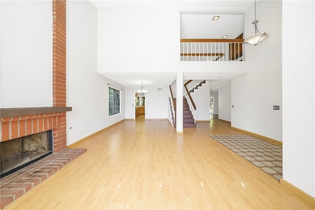 49 Village Loop Rd, Pomona, CA 91766 - unfurnished living room featuring wood finished floors, a chandelier, stairway, a brick fireplace, and a towering ceiling