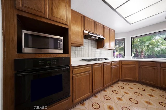 49 Village Loop Rd, Pomona, CA 91766 - kitchen with appliances with stainless steel finishes, under cabinet range hood, light countertops, brown cabinets, and backsplash