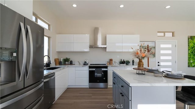 kitchen featuring white cabinets, appliances with stainless steel finishes, a breakfast bar, wall chimney range hood, and a sink