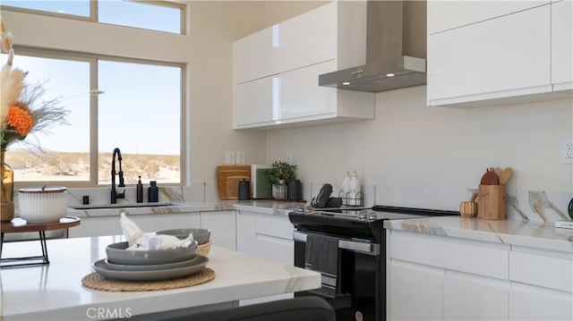 kitchen featuring electric stove, wall chimney range hood, a sink, and white cabinets