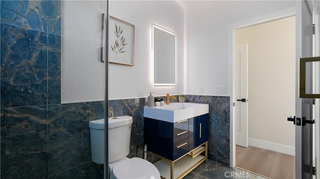 bathroom with wainscoting, toilet, wood finished floors, vanity, and tile walls