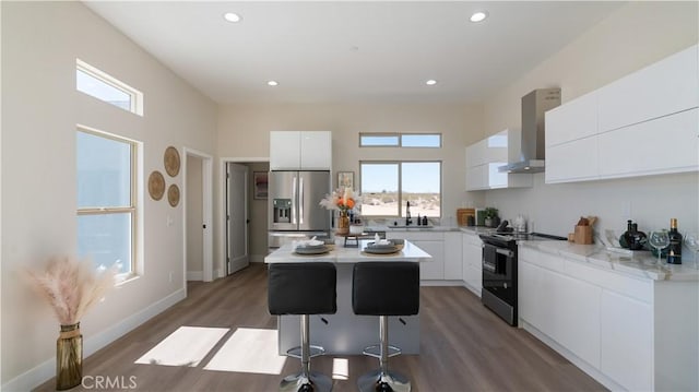 kitchen featuring a center island, stainless steel appliances, white cabinetry, a sink, and wall chimney range hood