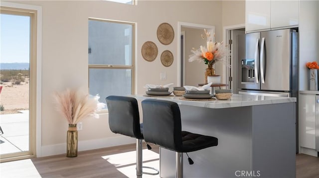 bar with baseboards, stainless steel fridge, and light wood finished floors