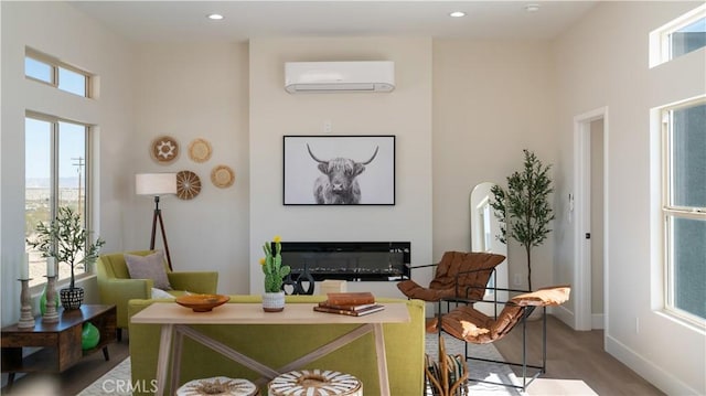 living area featuring recessed lighting, light wood-style floors, a glass covered fireplace, a wall mounted air conditioner, and baseboards