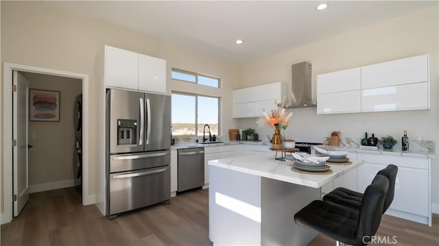 kitchen with a kitchen island, white cabinetry, light countertops, appliances with stainless steel finishes, and wall chimney range hood