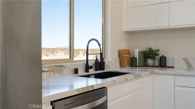 kitchen featuring stainless steel dishwasher, a sink, and white cabinetry