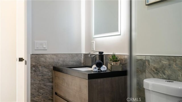 bathroom with toilet, a wainscoted wall, tile walls, and vanity