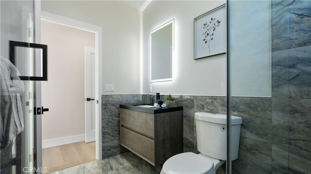 bathroom featuring toilet, a wainscoted wall, marble finish floor, vanity, and tile walls