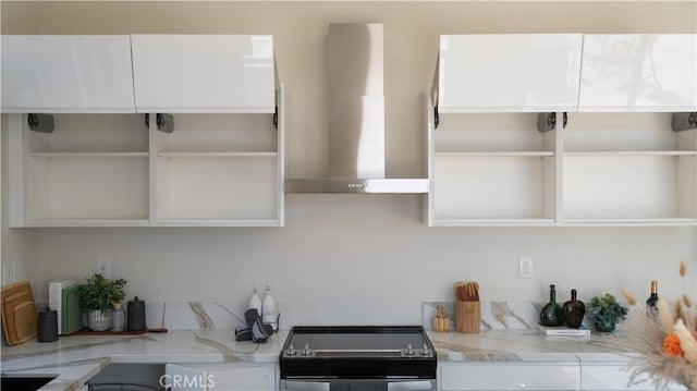 kitchen featuring wall chimney exhaust hood, electric range, open shelves, and light stone counters