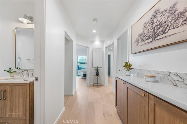 corridor with baseboards, a sink, and light wood-style floors