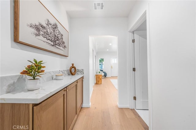 corridor with visible vents, baseboards, and light wood finished floors