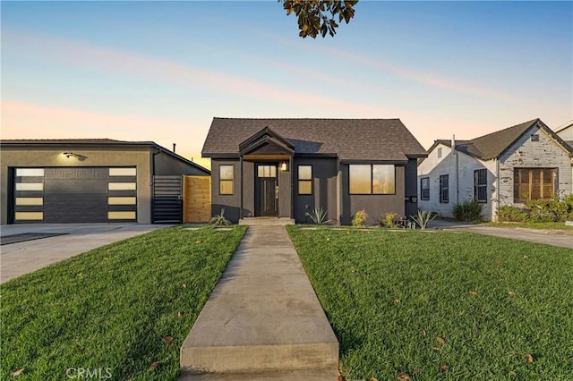 contemporary house featuring stucco siding, a lawn, a garage, and roof with shingles