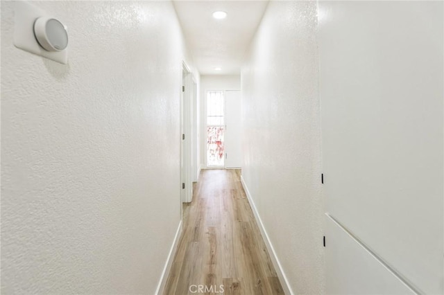 corridor featuring a textured wall, baseboards, and light wood-type flooring