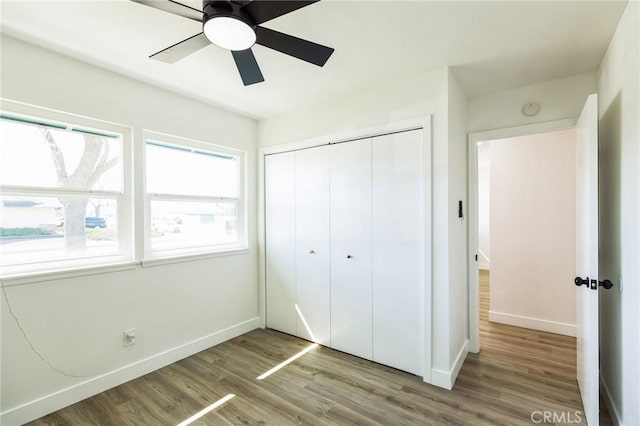 unfurnished bedroom featuring a ceiling fan, wood finished floors, a closet, and baseboards