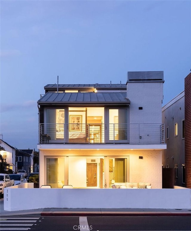 rear view of house with stucco siding, a standing seam roof, roof mounted solar panels, metal roof, and a balcony