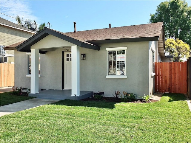 bungalow with a shingled roof, fence, a front lawn, and stucco siding