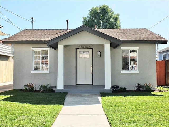 bungalow-style house featuring roof with shingles, a front yard, fence, and stucco siding