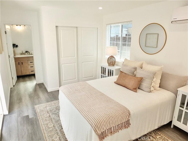 bedroom featuring a wall unit AC, recessed lighting, a closet, wood finished floors, and baseboards