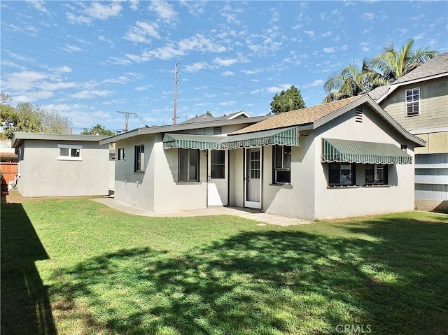 rear view of house featuring a lawn and stucco siding