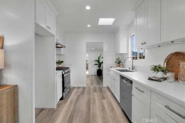 kitchen featuring a skylight, white cabinets, stainless steel appliances, under cabinet range hood, and a sink