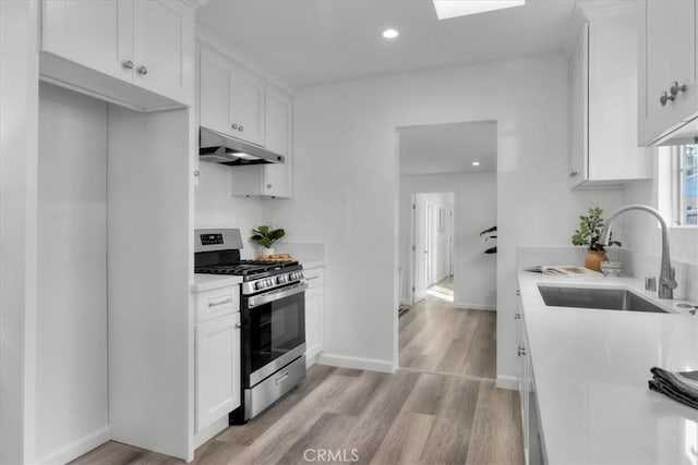 kitchen with under cabinet range hood, a sink, white cabinets, light countertops, and gas stove