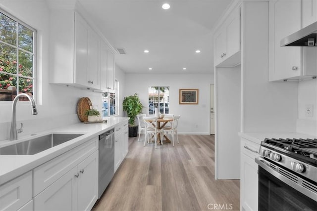 kitchen with stainless steel appliances, light countertops, white cabinetry, a sink, and wall chimney exhaust hood