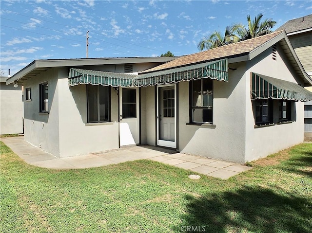 rear view of property with roof with shingles, a lawn, and stucco siding