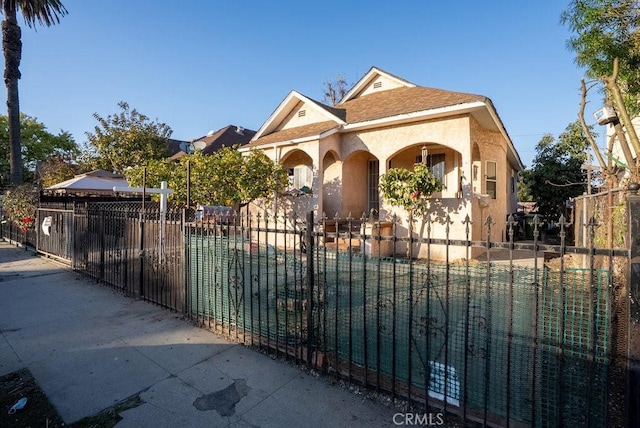 view of front of house featuring a fenced front yard, roof with shingles, and stucco siding