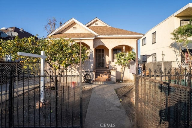 view of front of house featuring a fenced front yard, a gate, roof with shingles, and stucco siding