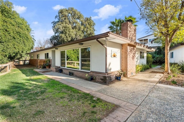 exterior space featuring brick siding, a front yard, a chimney, and stucco siding