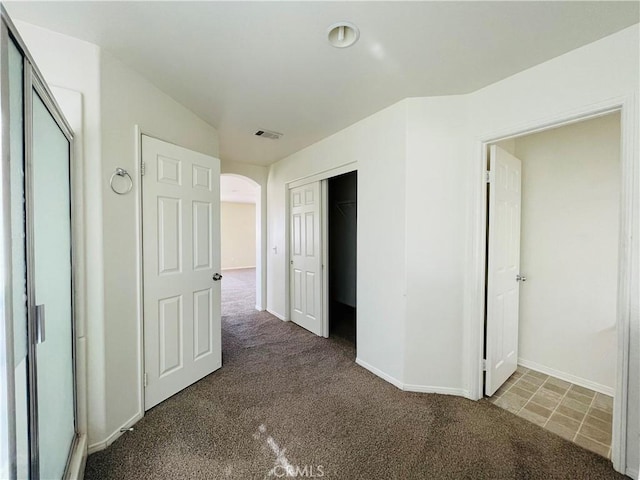 unfurnished bedroom with arched walkways, carpet flooring, visible vents, and baseboards