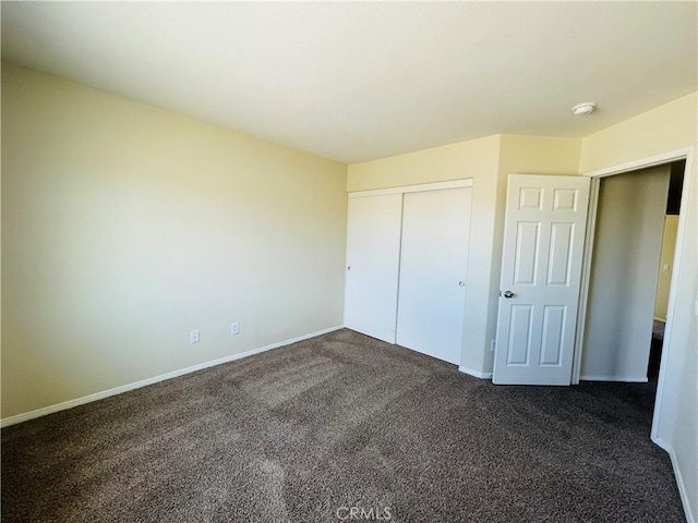 unfurnished bedroom featuring dark colored carpet, a closet, and baseboards