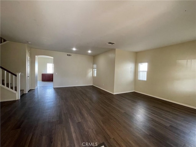 unfurnished living room featuring arched walkways, dark wood-style flooring, stairs, and visible vents