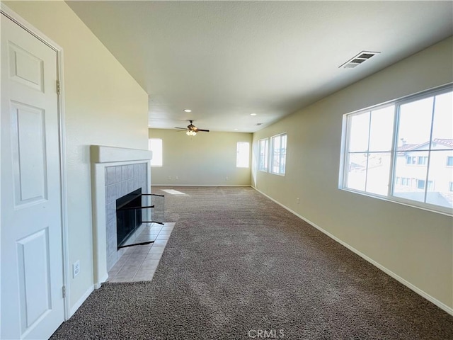 unfurnished living room with visible vents, a tiled fireplace, light carpet, ceiling fan, and baseboards