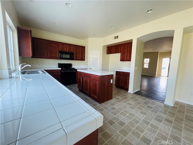 kitchen featuring light countertops, visible vents, a sink, a kitchen island, and black appliances