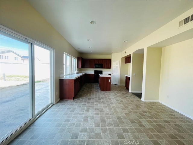 kitchen with light countertops, visible vents, open floor plan, a kitchen island, and black microwave